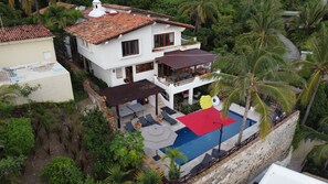 A two-story house with a swimming pool, surrounded by lush greenery and palm trees. - Private Beach- Amazing Surf- Pool -Staff - Gated Home- Suburban & Chef Available (Punta Mita)