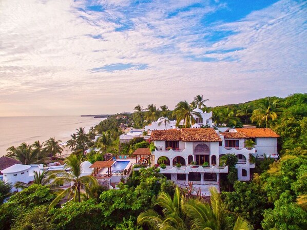 A coastal villa with multiple balconies, a swimming pool, and lush greenery. - Private Beach- Amazing Surf- Pool -Staff - Gated Home- Suburban & Chef Available (Punta Mita)