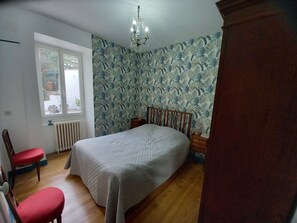 A bedroom with a wooden bed, a window with a view, a radiator, and a red chair.