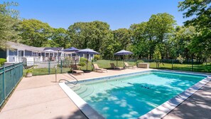 A swimming pool with lounge chairs and umbrellas, surrounded by a fenced area and trees.