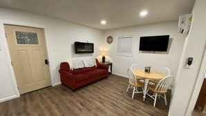 A compact living space with a red sofa, a dining table with chairs, a TV mounted on the wall, and a door with a window.