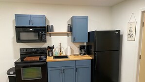 A compact kitchen with blue cabinets, a black refrigerator, a microwave, a stove, and a coffee maker.