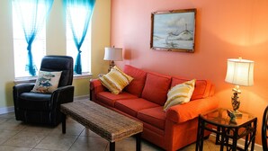 A living room with a sofa, armchair, and bench, a painting on the wall, and a lamp on a side table. - Serene is spending a day in this condo (Rockport)
