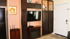 A living room with a flat-screen TV, wooden cabinets, a fireplace, and a door. - Serene is spending a day in this condo (Rockport)