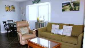 A living room with a leather armchair, a green sofa, and a glass-top coffee table. - Corner condo with bay window overlooking pool (Rockport)