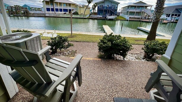 A waterfront view with a pool, outdoor seating, and buildings with balconies.