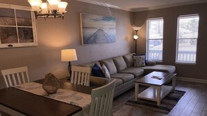 A cozy living room with a sofa, a dining table with chairs, and a lamp. - Beautiful Ground Level Condo (Rockport)