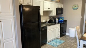 A compact kitchen with white cabinets, a black refrigerator, a microwave, and a sink. - Beautiful Ground Level Condo (Rockport)