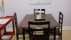 Un comedor con una mesa de madera, cuatro sillas, una araña y un cuadro en la pared.