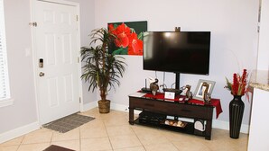 Un salon avec un téléviseur posé sur un meuble, une plante en pot, un tableau et un vase rempli de fleurs.