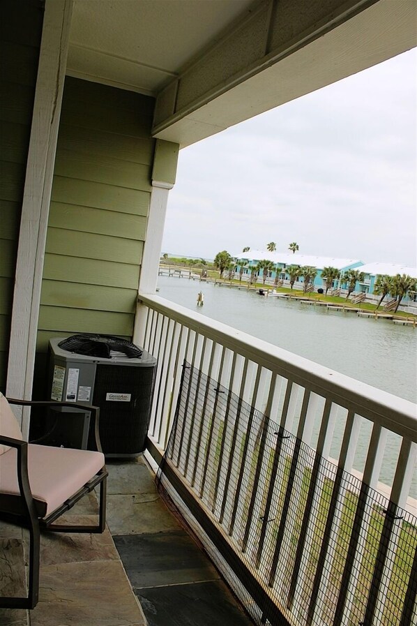 A balcony with a view of a water body, a trash can, and a chair.