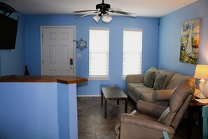 A living room with a sofa, a coffee table, a ceiling fan, and a painting on the wall.