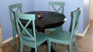 Un coin repas avec une table ronde et quatre chaises, deux tableaux accrochés au mur et un luminaire au plafond.