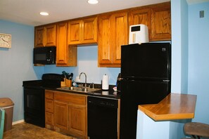 A kitchen with wooden cabinets, a microwave, a black refrigerator, a dishwasher, and a wooden table.