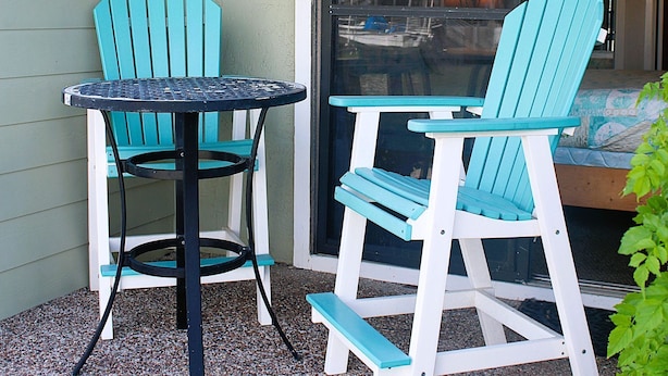 Eine Terrasse mit zwei Adirondack-Stühlen und einem kleinen runden Tisch.