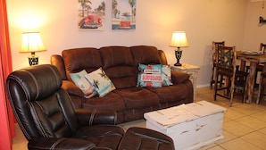 Ein Wohnzimmer mit braunem Ledersofa, zwei Sesseln, einem Esstisch mit Stühlen und zwei Wandleuchten.