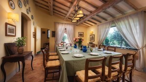 Comedor con una mesa larga dispuesta para seis personas, sillas de madera, un jarrón de flores y vistas a través de la ventana.