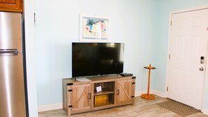 Una cocina con un refrigerador de acero inoxidable, un armario de madera con un televisor de pantalla plana y una puerta con felpudo.