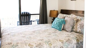 Un dormitorio con cama, ventilador de techo, ventana con cortinas, una silla y una lámpara.