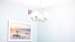 A dining area with a white table, four white chairs, a chandelier, a framed picture on the wall, and a vase with flowers on the table. - Second floor condo with canal view (Rockport)