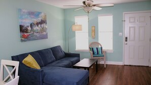 A living room with a blue sofa, a white chair, a small table, a ceiling fan, and a door. - Second floor condo with canal view (Rockport)