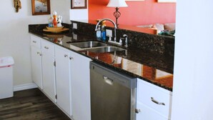Una cocina con armarios blancos, lavavajillas, encimera de granito y pileta.