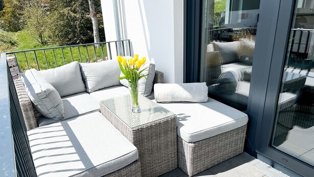 A balcony with wicker furniture, a glass table, and a vase with yellow flowers. - Gemütliche & Luxuriöse Ferienwohnung in Top-lage (Höchenschwand)