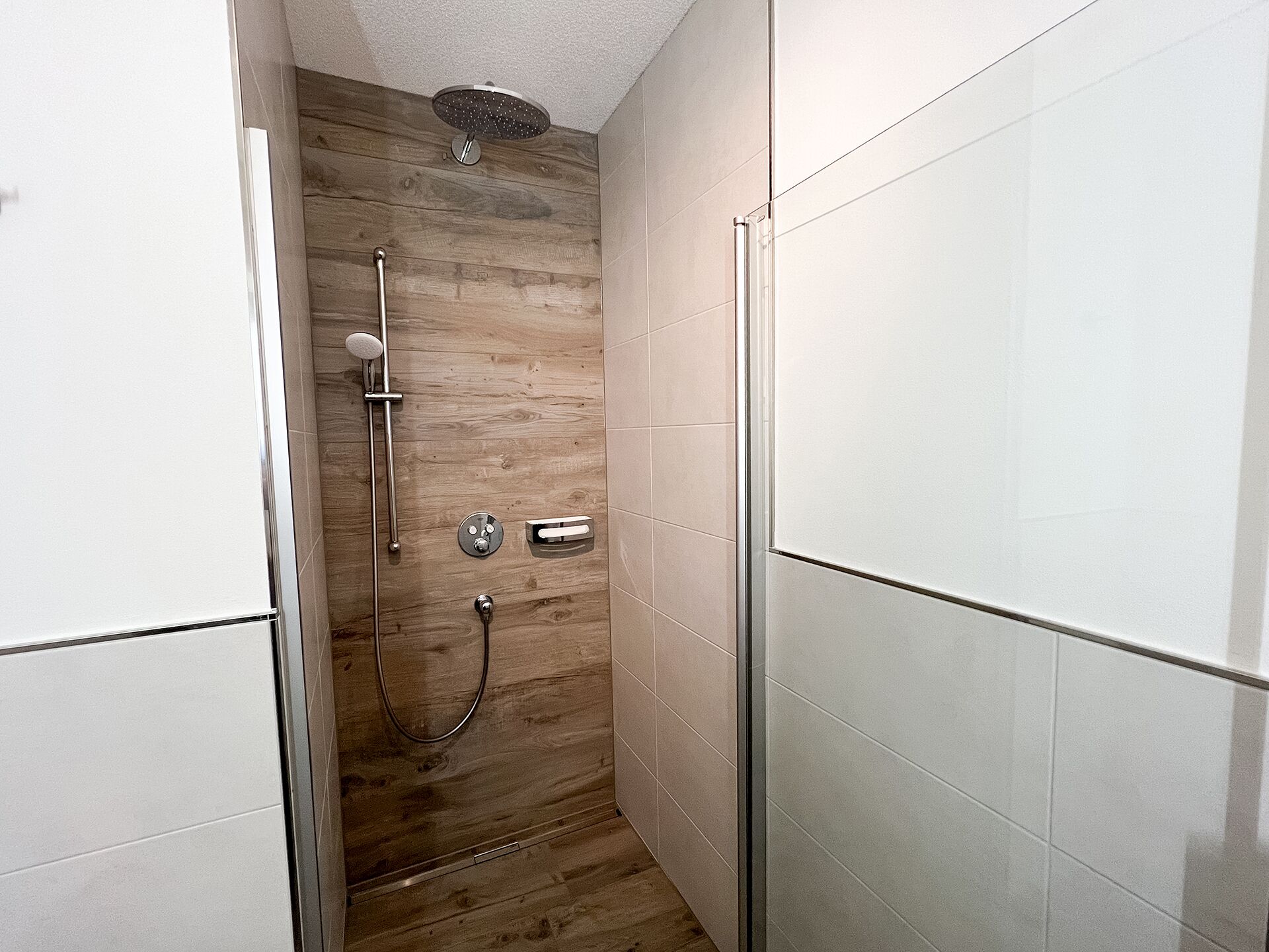 Een moderne douche met een wandpaneel van hout, een handdouche en een muurbevestigde kraan.