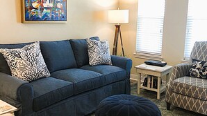 A living room with a blue sofa, patterned cushions, a floor lamp, a side table, and a painting on the wall. - Fantastic water view from comfortable cozy condo (Rockport)