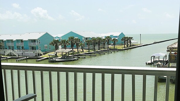 A waterfront view with a balcony, a pier, and buildings with a consistent architectural style. - Fantastic water view from comfortable cozy condo (Rockport)