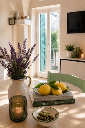 A table with a vase of lavender, a bowl of lemons, and a bowl of olives, with books and a candle. - A charming old Virginia home with a garden and ocean views (Cervo)
