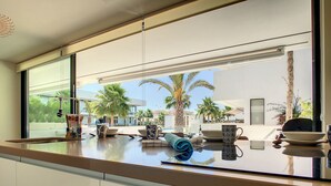 A modern kitchen with a large window overlooking a pool and palm trees. - Modern, large terrace, pool and BBQ (Mar de Cristal)