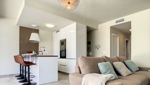A modern living room with a beige sofa, a coffee table, and a kitchen in the background. - Modern, large terrace, pool and BBQ (Mar de Cristal)