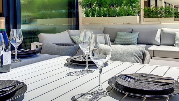 A modern outdoor dining area with a table set for two, large windows, and a sofa with cushions. - Modern, large terrace, pool and BBQ (Mar de Cristal)
