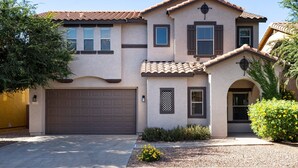 A two-story house with a brown garage door, a small porch with a curved roof, and a landscaped front yard with a tree and shrubs. - "THE HAMPTON" Gilbert I Designer Style + Comfort I 3bed/2.5bath (Gilbert)