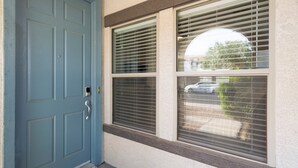 A blue door with a silver handle, a window with horizontal blinds, and a small window with a view of a car and trees. - "THE HAMPTON" Gilbert I Designer Style + Comfort I 3bed/2.5bath (Gilbert)
