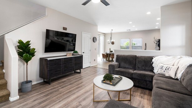 A modern living room with a flat-screen TV, dark sofa, coffee table, and a ceiling fan. - "THE HAMPTON" Gilbert I Designer Style + Comfort I 3bed/2.5bath (Gilbert)