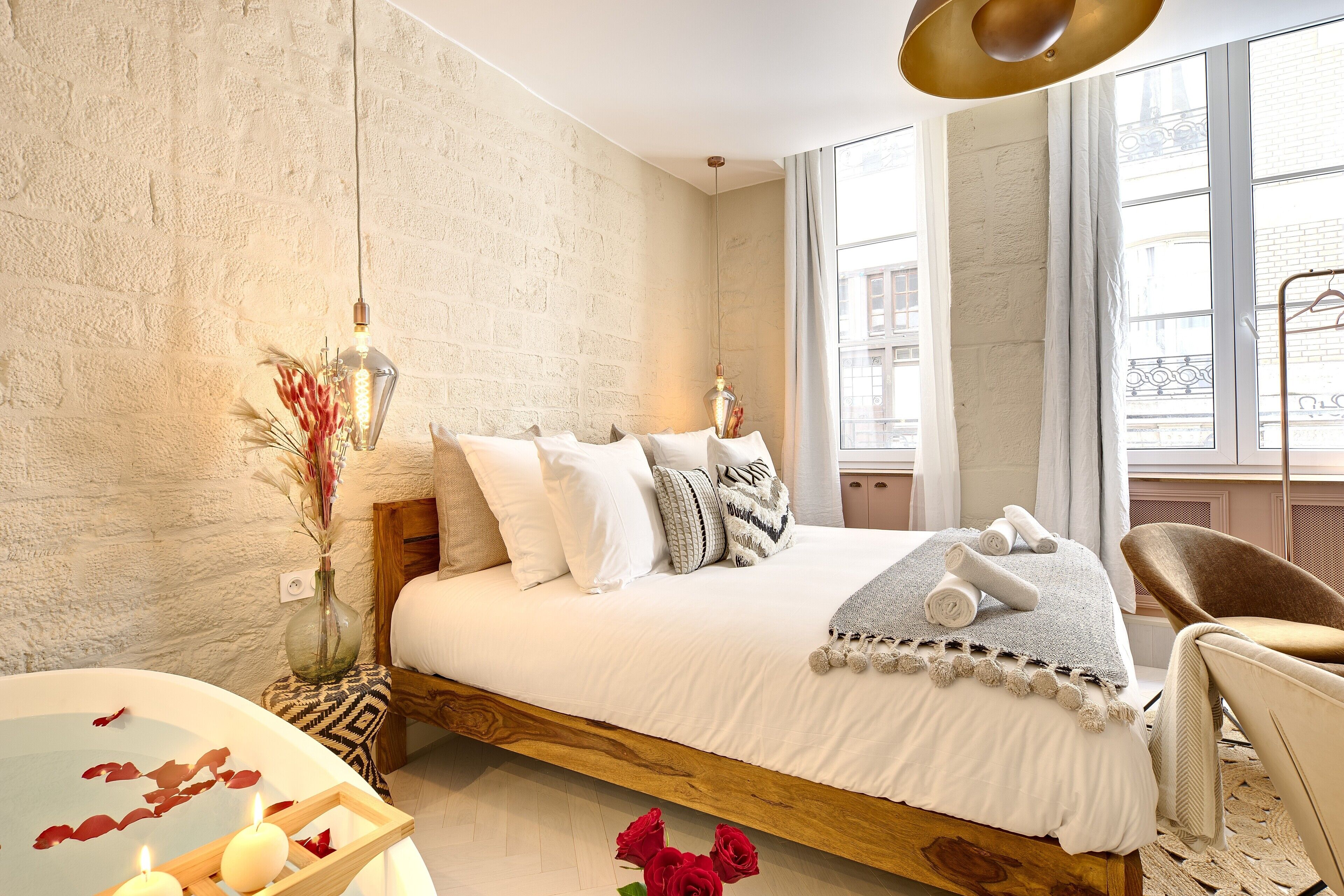 A bedroom with a large bed, a wooden headboard, a bedside table with candles, and a view of the city through the window.