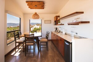 Cozinha com armários de madeira, mesa de jantar com cadeiras, vista para vinhedos e luminária pendente.