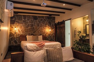 A bedroom with a stone wall, a wooden bed frame, and a bedside table with a lamp.