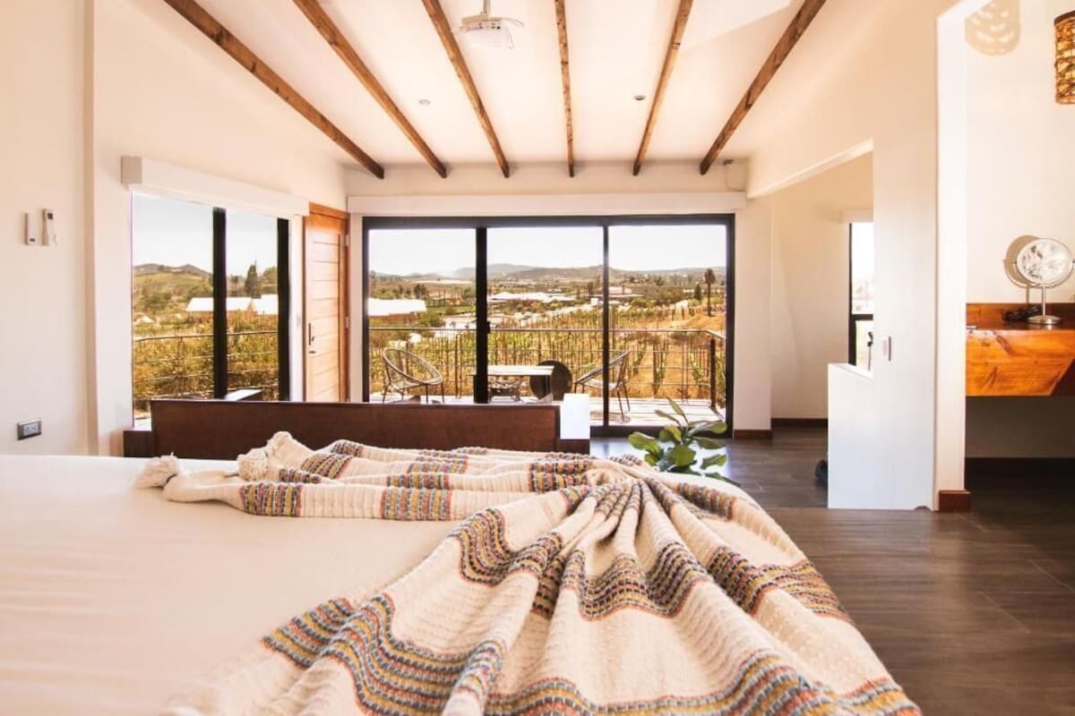 A bedroom with a large bed, a view of vineyards, and a balcony with chairs.