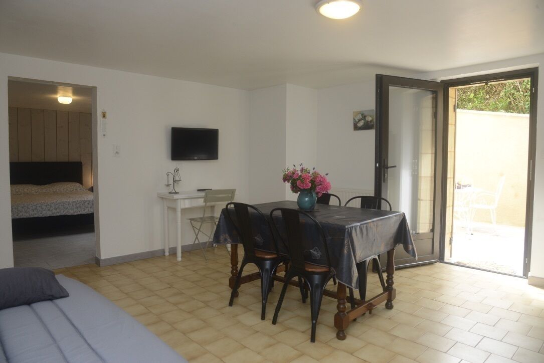 Un espace de vie compact comprenant un coin repas, un lit, un téléviseur et une porte-fenêtre coulissante donnant sur un espace extérieur.