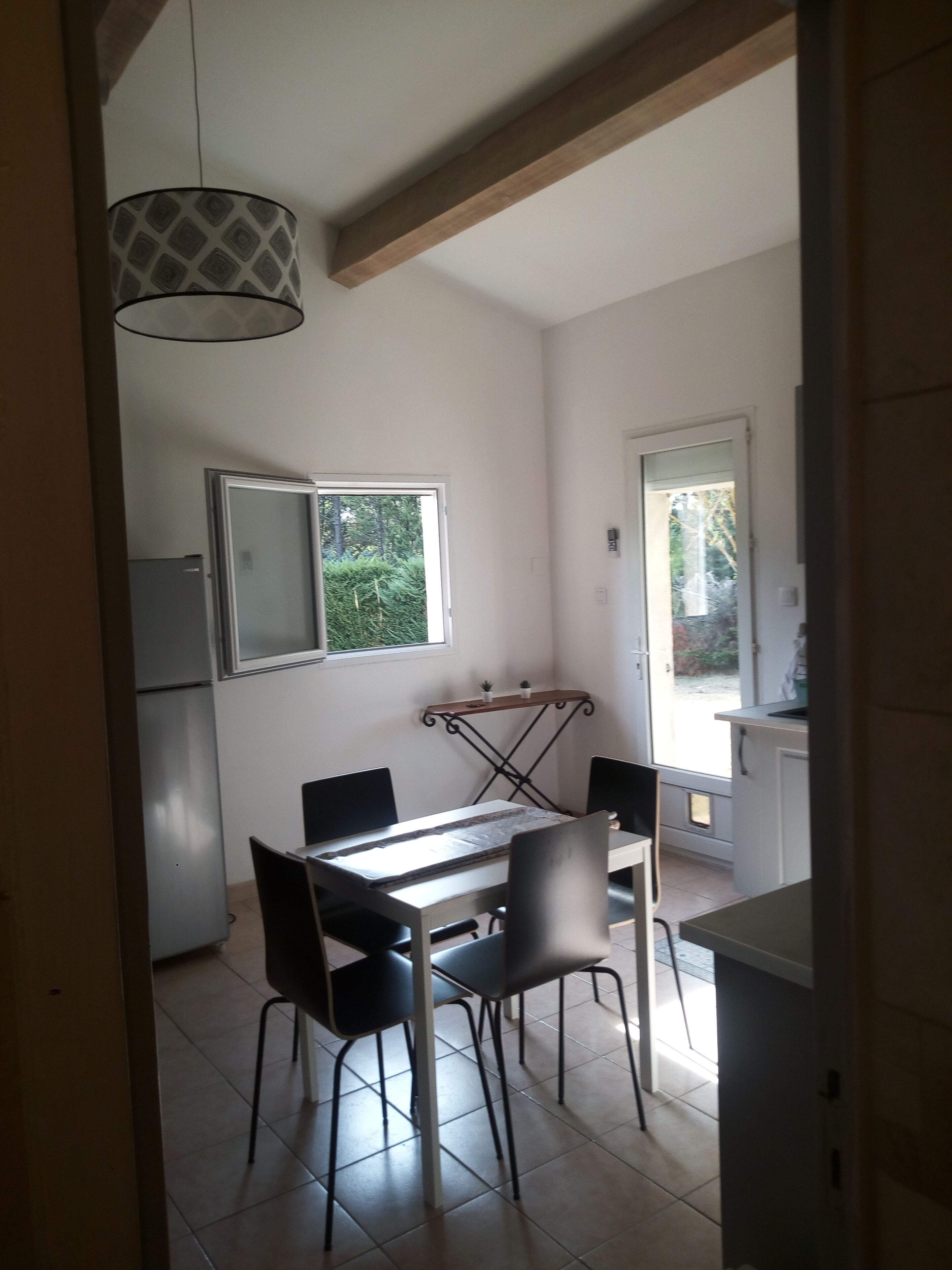 A compact kitchen with a dining area, featuring a table with chairs, a hanging light fixture, and a window providing natural light.