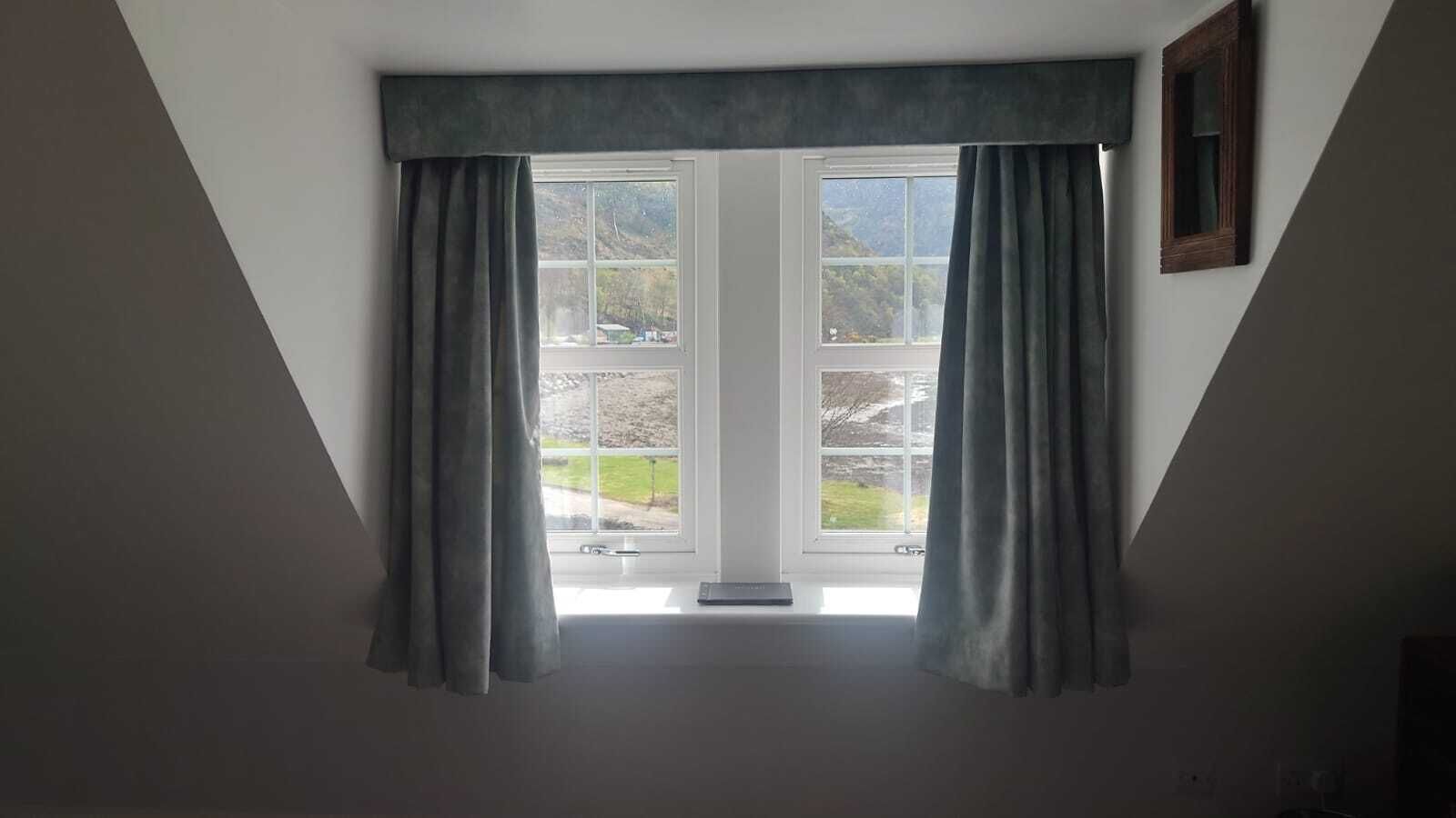 A room with a large window, a white ceiling, and a dark-colored curtain.