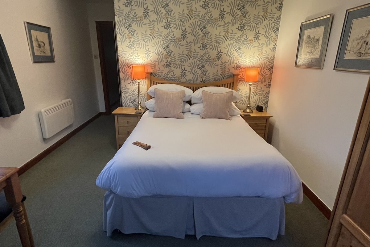 A hotel room with a large bed, two bedside lamps, a wooden nightstand, and a radiator.