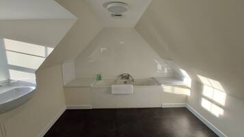 A spacious attic bedroom with a large skylight, a built-in bathtub, and a dark floor.