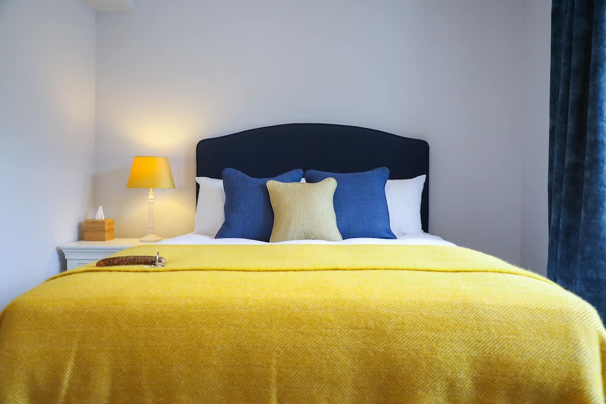 A neatly made bed with a yellow blanket, a dark headboard, and two pillows in blue and beige.