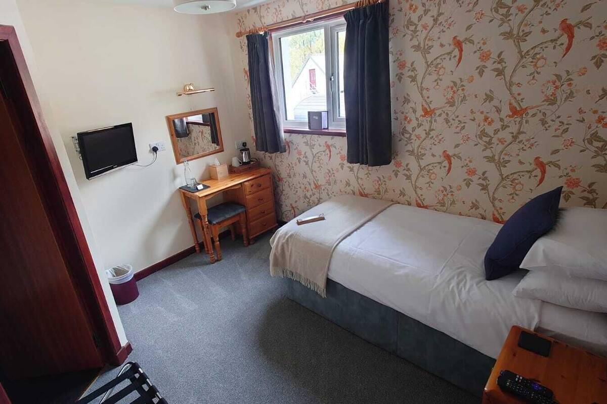 A bedroom with a bed, a desk, a chair, a mirror, and a window with curtains.