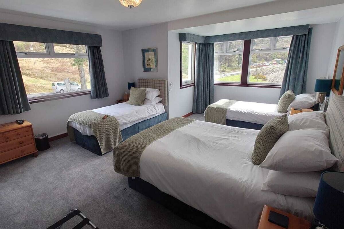 A bedroom with two single beds, a wooden dresser, and a window with curtains.