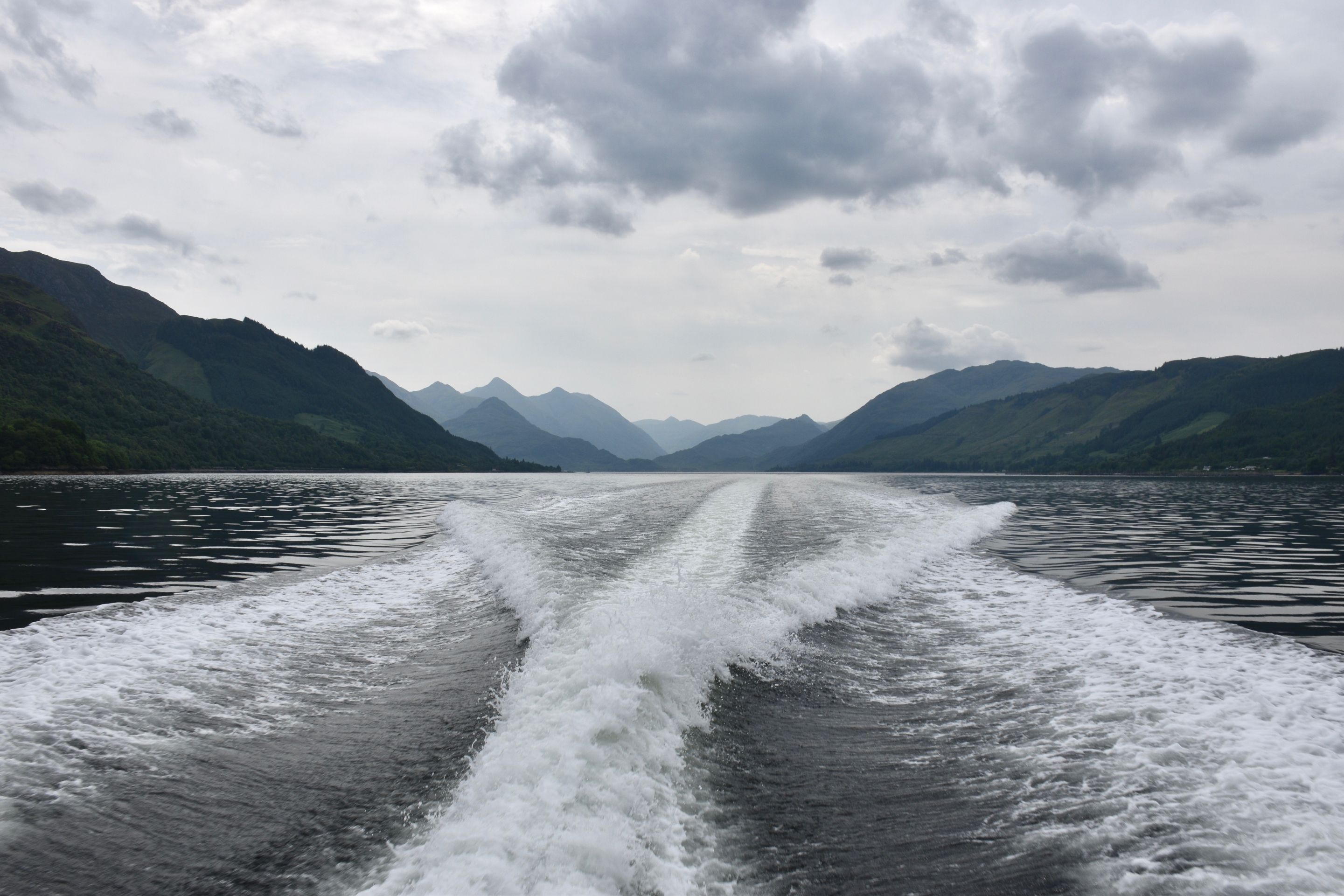 A boat's wake on a lake with mountains in the background.